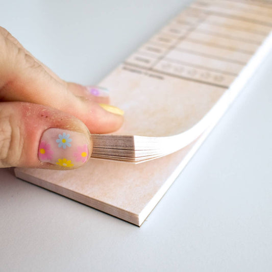 Hand with floral nail art holding a wooden block with a clear plastic sheet over it.