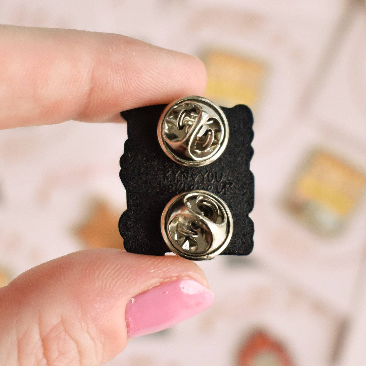Back side of enamel pin with double safety pins held by a hand