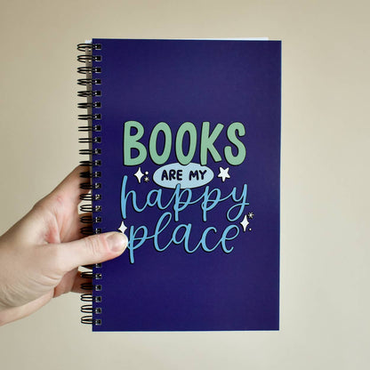 Notebook with 'Books are my happy place' text held by a hand against a beige background