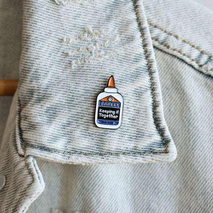 Enamel pin attached to denim jacket pocket, featuring glue bottle with humorous message