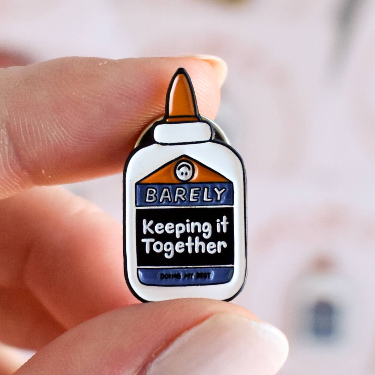 Enamel pin of glue bottle with text 'Barely Keeping It Together' 