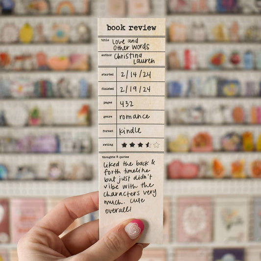 Hand holding a book review card with a blurred bookshelf background