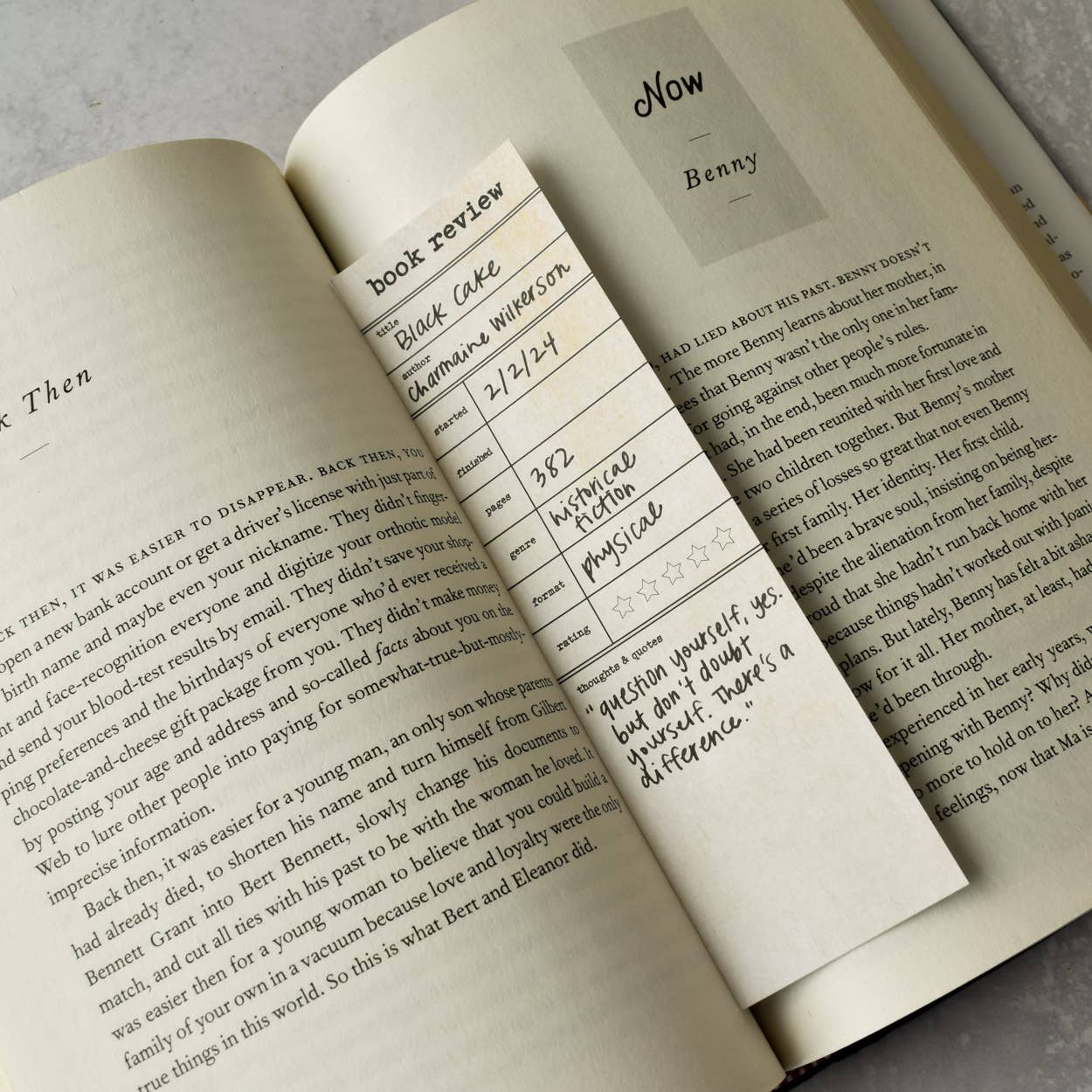 Open book with a bookmark featuring text and a name card on a gray surface