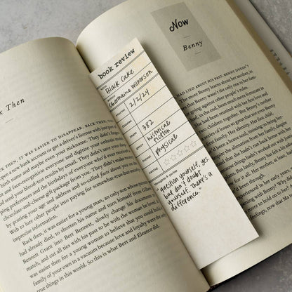 Open book with a bookmark featuring text and a name card on a gray surface