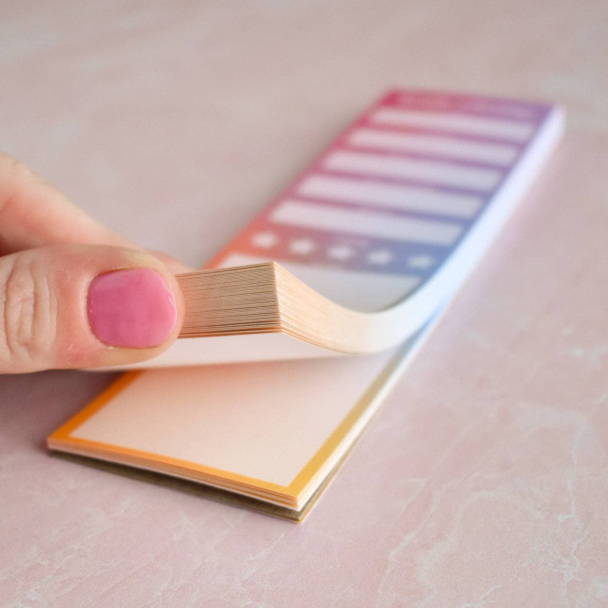 Hand holding a small book review notepad bookmark on a light pink background