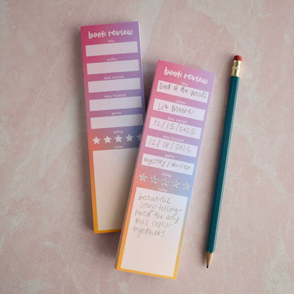 Two book review notepads with a pencil on a pink surface